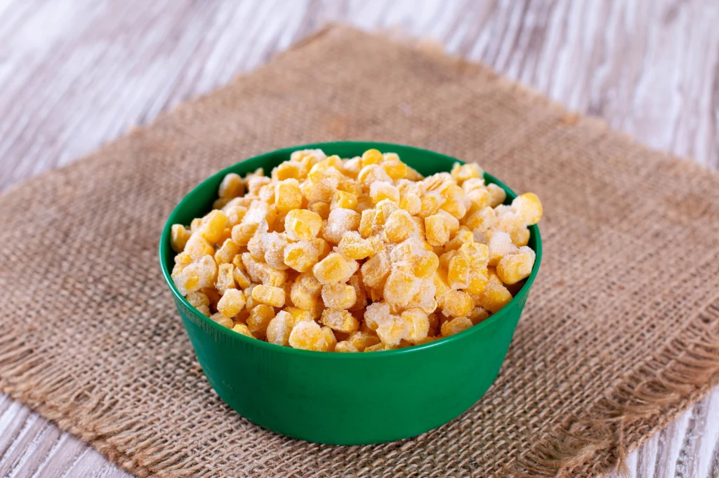 Warto sięgać po kukurydzę w kolbie lub mrożoną Zielona miska wypełniona mrożoną kukurydzą ustawiona na jutowej podkładce na drewnianym stole.