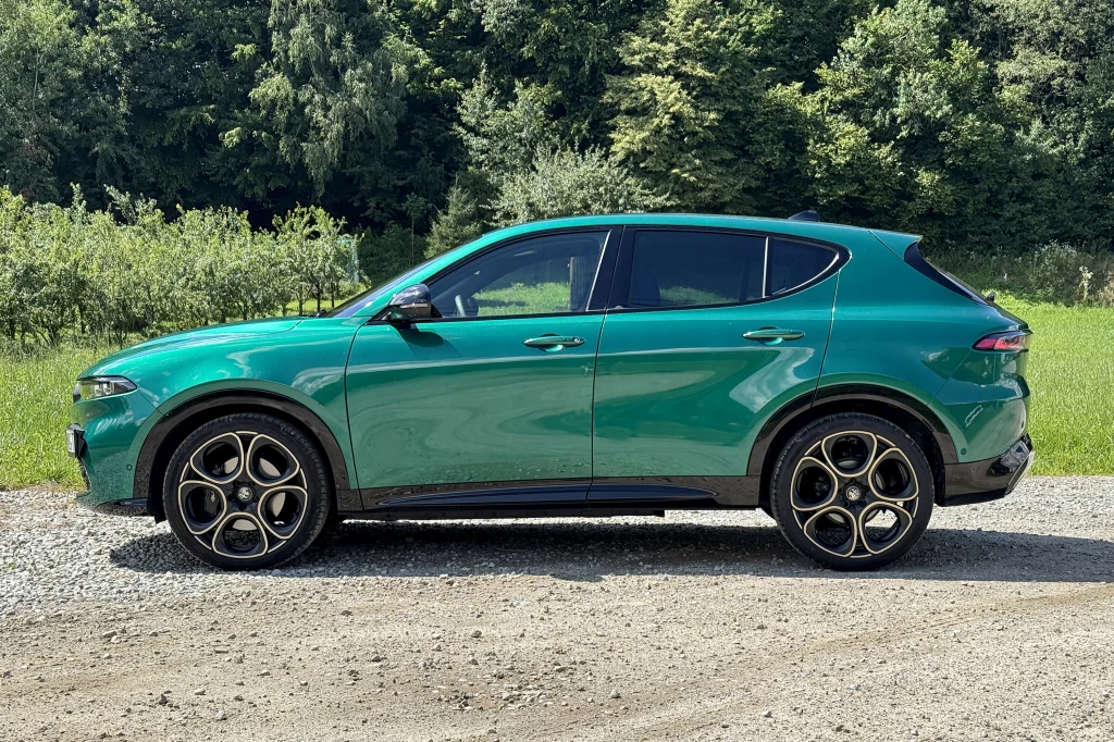 Alfa Romeo Tonale ma 453 cm długości Zielony samochód typu SUV zaparkowany na żwirowej drodze, otoczony bujną zieloną roślinnością i drzewami w tle.