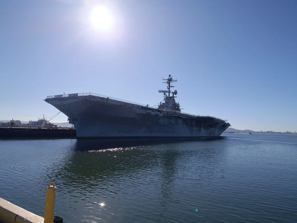 USS Hornet u wybrzeży Alamedy. W czasie wojny przy pełnym obciążeniu osiągał wyporność rzędu 37 tys. ton Lotniskowiec zacumowany w spokojnym porcie przy słonecznej pogodzie, na wodzie odbijają się promienie słońca, widoczny fragment nabrzeża.