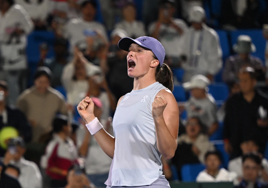 Iga Świątek Tenisistka w sportowym stroju wyraża radość i triumf, stojąc na tle widowni pełnej kibiców, którzy okazują entuzjastyczne wsparcie.