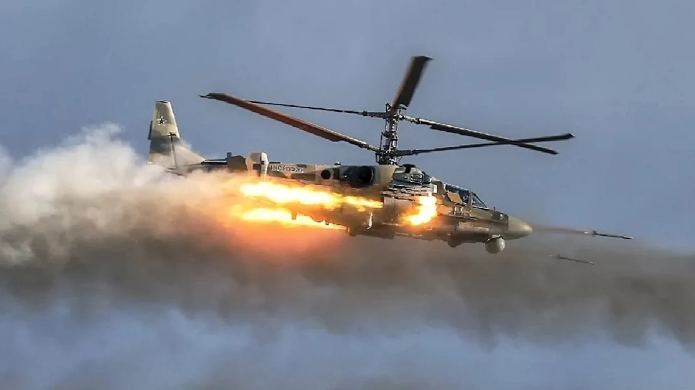 Ukraińcy zniszczyli już 64 potężne rosyjskie śmigłowce Ka-52 Aligator Śmigłowiec bojowy wystrzeliwuje pociski w trakcie lotu, intensywny płomień i dym towarzyszą rakietom, tło stanowi niebo o jednolitym, lekko zachmurzonym zabarwieniu.