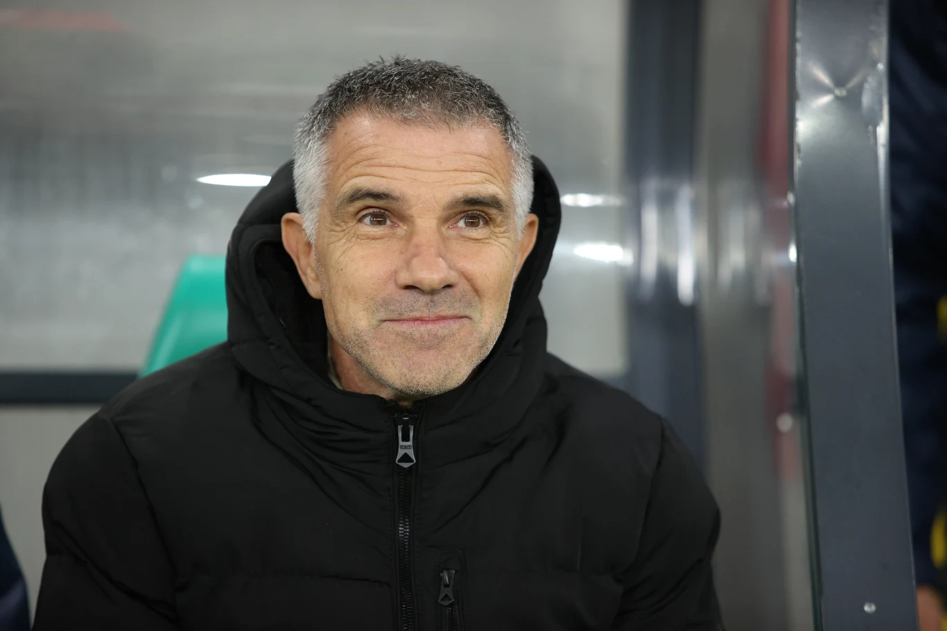 Trener krakowskiego zespołu, Gino Lettieri, przed pierwszym gwizdkiem był dobrej myśli Mężczyzna z krótkimi, siwiejącymi włosami i zarostem siedzi na ławce ubrany w czarną kurtkę, patrząc lekko w bok i delikatnie się uśmiechając.