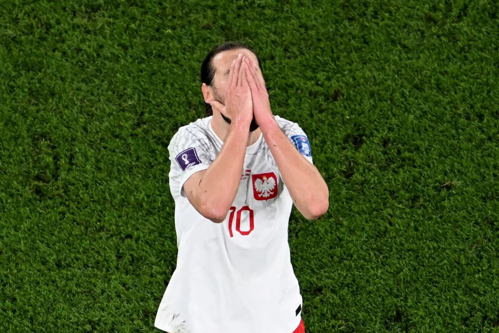 Grzegorz Krychowiak w reprezentacji Polski Piłkarz w białej koszulce z orłem i numerem 10 na boisku trawiastym trzyma ręce na twarzy w geście rozczarowania lub smutku.