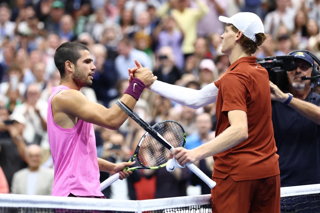 Carlos Alcaraz i Jannik Sinner to dwaj faworyci do triumfu w ATP Finals 2025 Dwóch tenisistów ściska sobie dłonie nad siatką po zakończonym meczu, na tle tłumu kibiców i kamerzysty, atmosfera pełna sportowych emocji i wzajemnego szacunku.