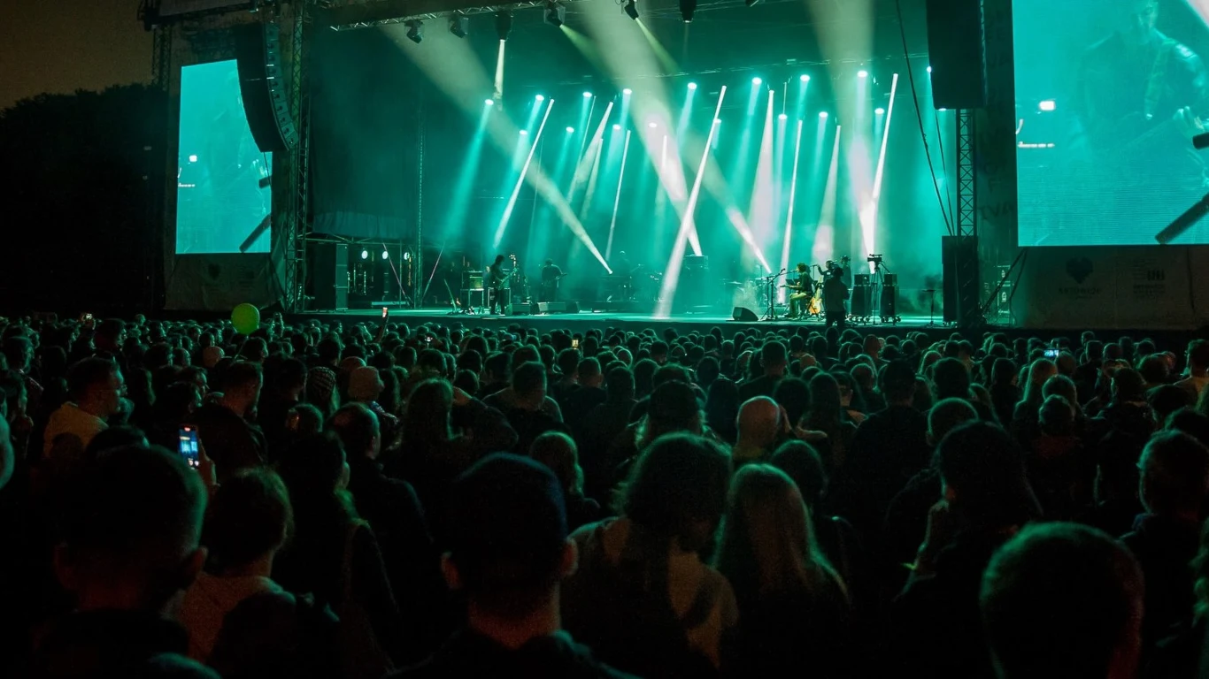 Nowy festiwal pojawił się na mapie Polski! Tłum ludzi zgromadzony przed dużą sceną koncertową, oświetloną intensywnym, zielonym światłem, na scenie widoczni muzycy grający podczas plenerowego wydarzenia muzycznego.