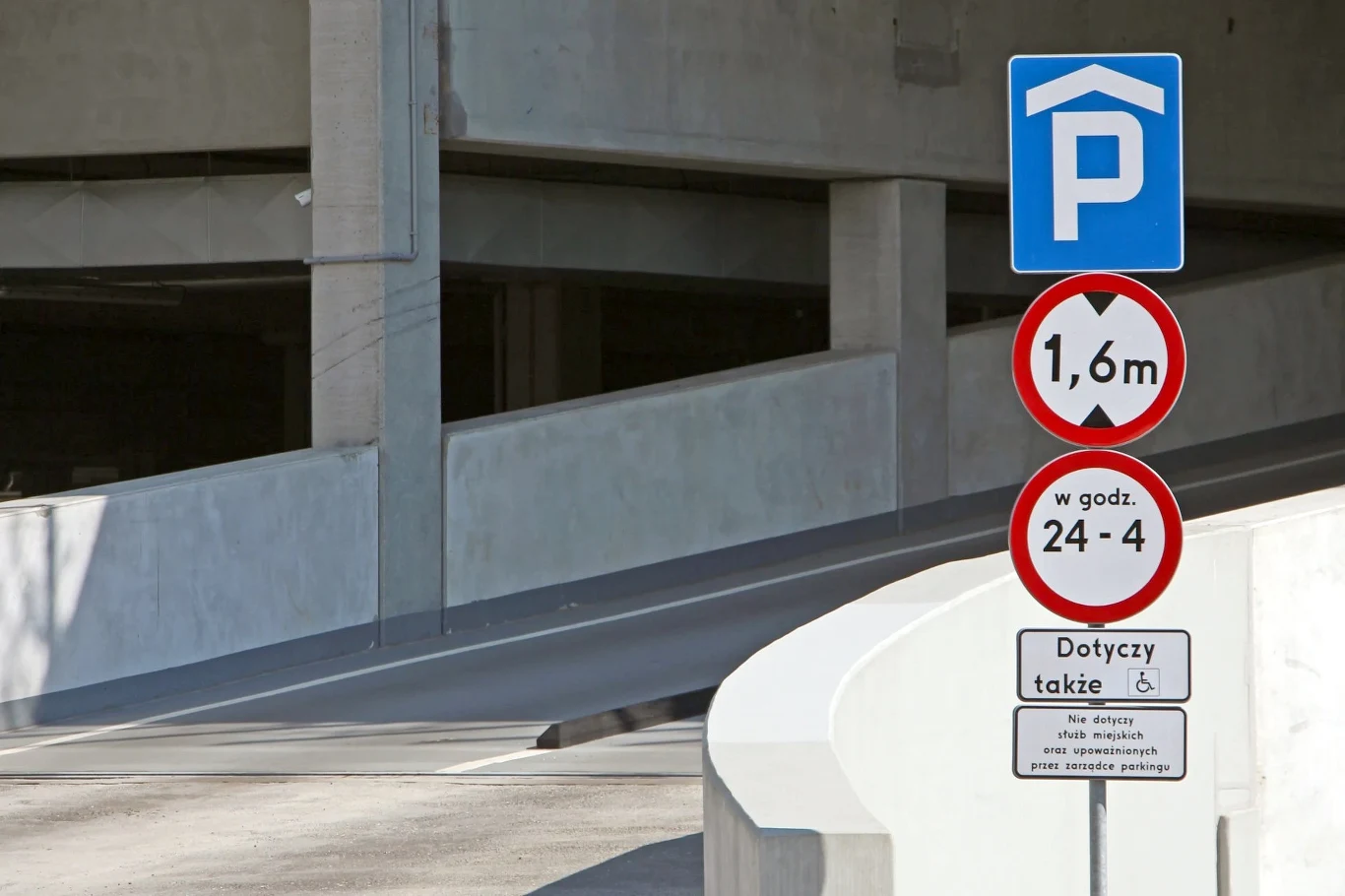 Znak B-16 określa dopuszczalną wysokość pojazdu. Ale przepisy przewidują spory margines bezpieczeństwa Wjazd do parkingu wielopoziomowego z oznaczeniem ograniczenia wysokości do 1,6 metra oraz informacją o godzinach obowiązywania ograniczenia i dotyczących osób niepełnosprawnych.