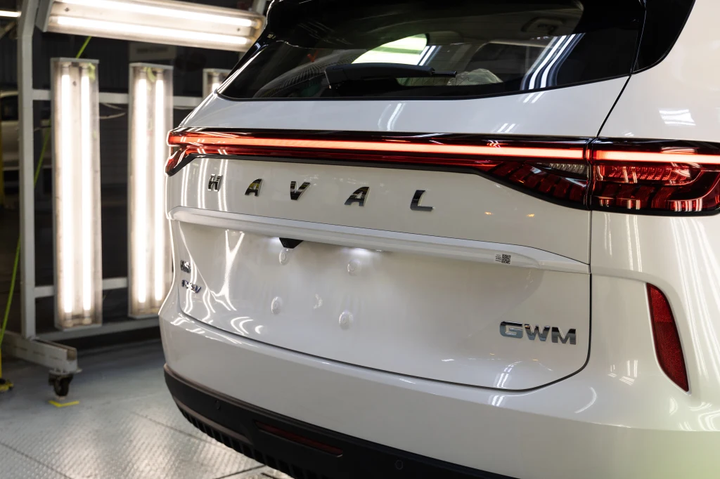 Great Wall Motors planuje poszerzyć gamę modeli w Europie. Tylna część białego samochodu marki Haval z oznaczeniem GWM, ustawiona w oświetlonym pomieszczeniu technicznym, widoczne są lampy kontrolne oraz światło odbijające się od karoserii.