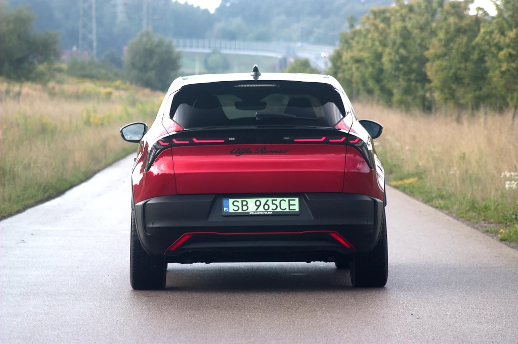 Czerwony samochód osobowy marki Alfa Romeo stoi na wąskiej asfaltowej drodze otoczonej zielenią i drzewami, widok z tyłu, na tablicy rejestracyjnej oznaczenie polskie.