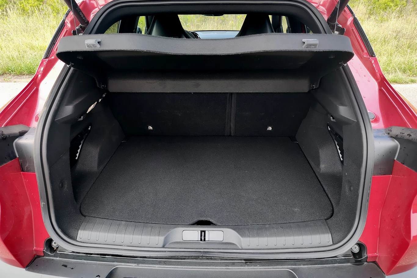 Alfa Romeo Junior Otwarty bagażnik czerwonego samochodu osobowego z przestronną, pustą przestrzenią ładunkową i podniesioną roletą bagażnika.