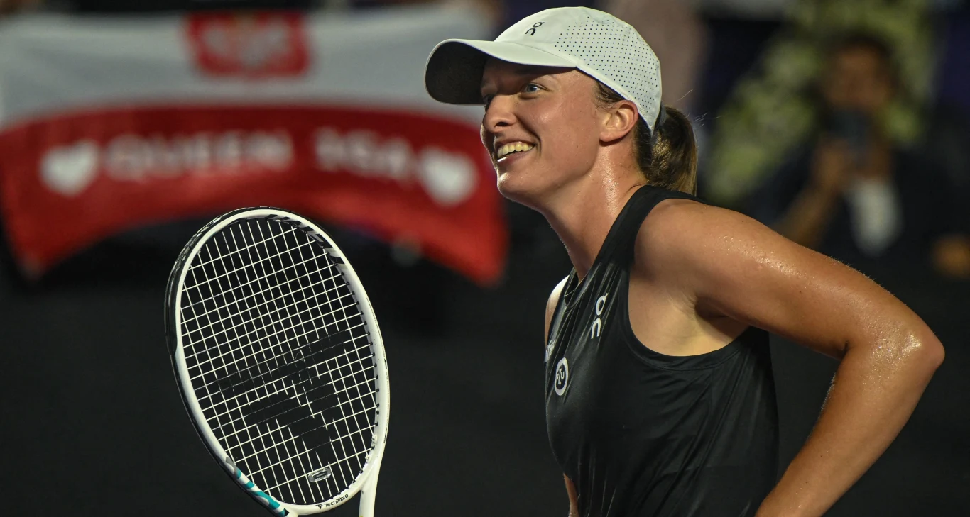 Iga Świątek Tenisistka w czarnej koszulce i białej czapce z rakietą w ręku uśmiecha się na korcie tenisowym. W tle widoczna polska flaga oraz napis Queen Iga.