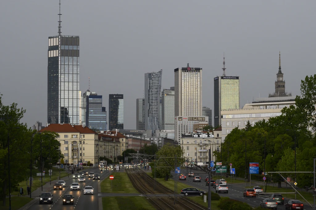 GUS: dobre dane na temat polskiego PKB (zdj. ilustracyjne) Warszawska panorama z nowoczesnymi wieżowcami i centrum miasta, ruchliwa ulica z samochodami i torami tramwajowymi otoczona zielenią po obu stronach.