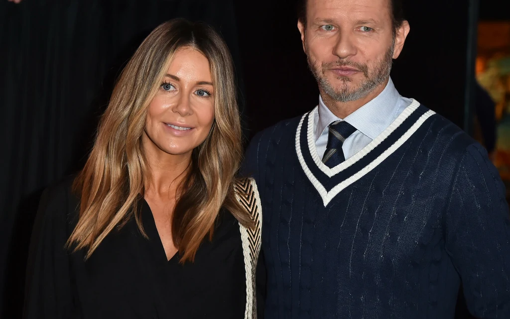 Małgorzata Rozenek i Radosław Majdan Dwie osoby pozujące razem, kobieta z długimi blond włosami w czarnej bluzce i mężczyzna w niebieskim swetrze z białymi wzorami, na tle ciemnego wnętrza.