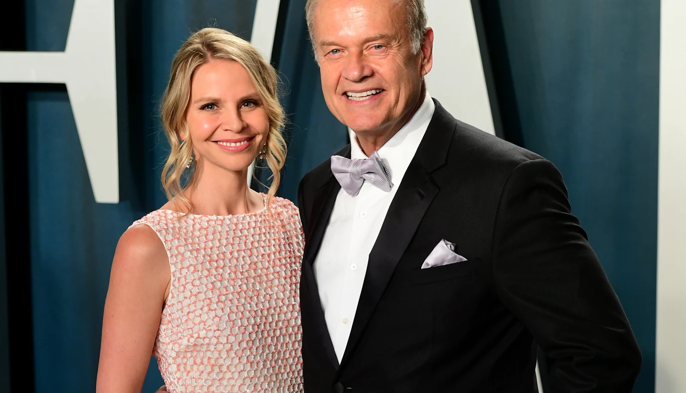 Kelsey Grammer i Kayte Walsh. Elegancka para ubrana w wieczorowe stroje, kobieta w jasnej sukni bez rękawów, mężczyzna w czarnym garniturze z muchą, oboje uśmiechnięci na tle ciemnej dekoracji.