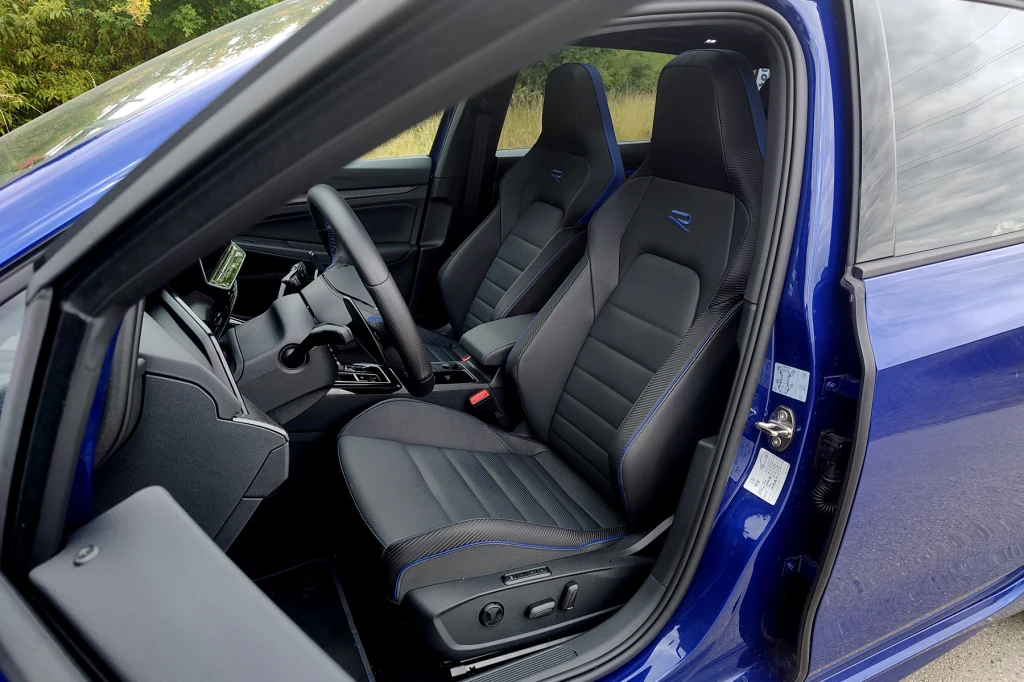 Pokryte skórą fotele wymagają dopłaty i to słonej Widok wnętrza nowoczesnego samochodu z naciskiem na przednie fotele pokryte skórą, ergonomicznie zaprojektowane, wyposażone w przeszycia i oznaczenie modelu, kokpit z elementami sterowania oraz wyświetlacze, otwarte drzwi po stronie kierowcy.