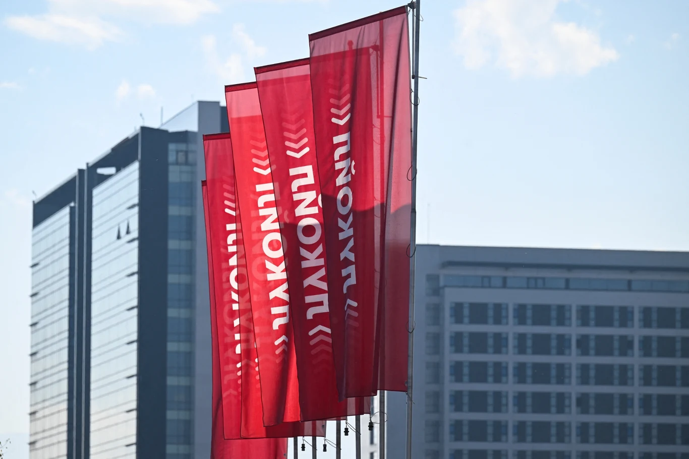 Amerykańskie sankcje boleśnie uderzają w Łukoil, a tym samym w ważne źródło przychodów Kremla Czerwone flagi z białym napisem ŁAKONI na tle nowoczesnych, szklanych budynków biurowych w słoneczny dzień