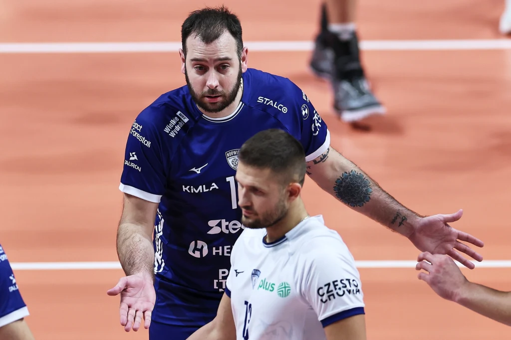 Luciano De Cecco, nowa gwiazda drużyny z Częstochowy Dwóch siatkarzy podczas meczu, jeden z nich w niebieskiej koszulce z gestem rozłożonych rąk, sugerującym niezadowolenie lub zdziwienie; drugi zawodnik w białej koszulce patrzy w dół, a w tle widać linię boiska.