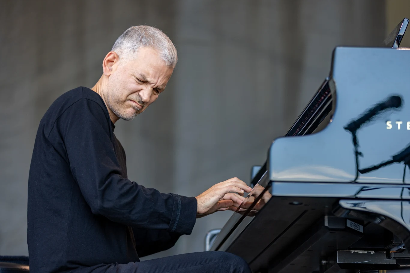 Brad Mehldau wystąpi w Katowicach w duecie z Christianem McBride'em Mężczyzna o siwych włosach w czarnym ubraniu gra na fortepianie, wyrażając emocje skupienia i pasji, na pierwszy plan wysuwa się elegancki fortepian koncertowy.
