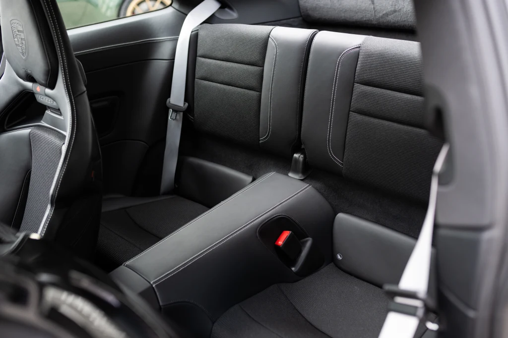 Tylne siedzenia nowoczesnego samochodu osobowego z widocznymi pasami bezpieczeństwa, ciemna tapicerka, wyraźne przeszycia i sportowy charakter wnętrza.