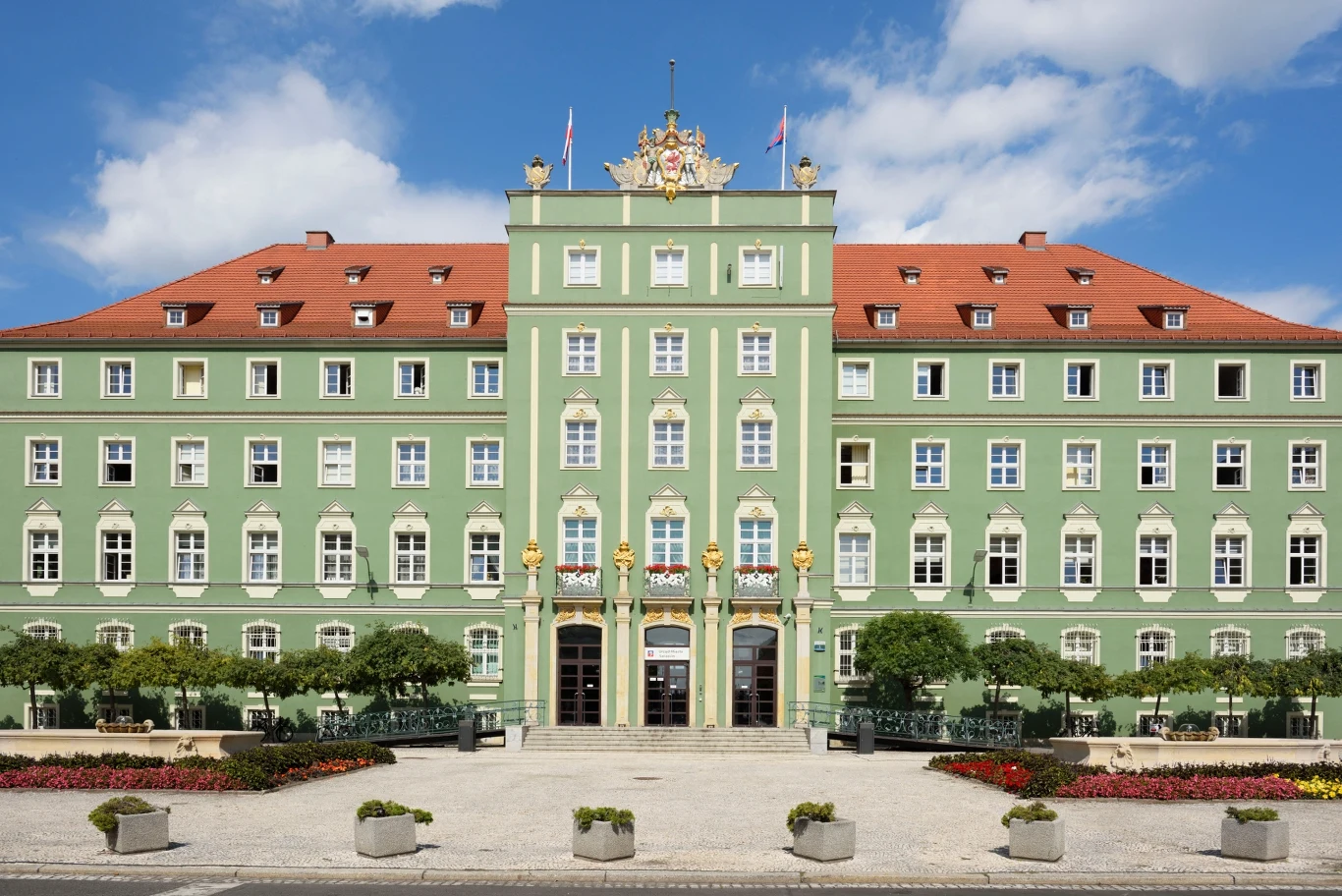 Szczecin pozwał Skarb Państwa o zwrot pieniędzy za wydatki oświatowe Zielony budynek o symetrycznej fasadzie z licznymi oknami, czerwonym dachem i bogato zdobionym wejściem, przed którym znajduje się plac z alejkami, roślinnością dekoracyjną i donicami. Nad wejściem herby i flagi.