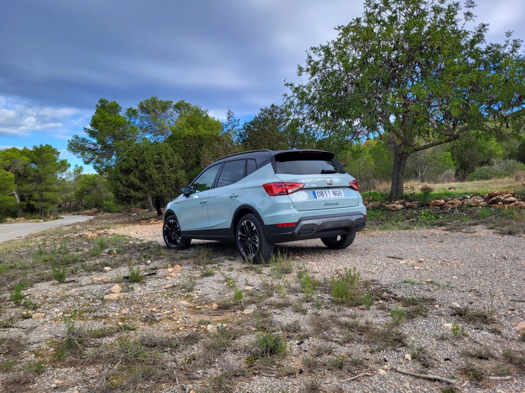 Podobnie jak Ibiza, także Arona będzie dostępna w trzech nowych kolorach nadwozia - Liminal, Oniric i Hypnotic. Jasnoniebieski samochód SUV zaparkowany na kamienistej, leśnej drodze, otoczony drzewami oraz zielenią leśną pod lekko zachmurzonym niebem.