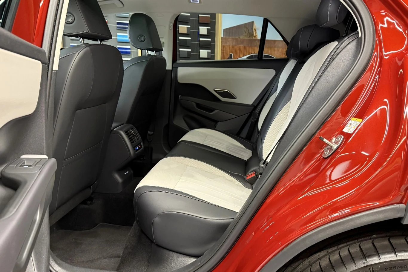 Przestronne tylne siedzenia z jasną i ciemną tapicerką, otwarte drzwi samochodu, widoczne elementy przednich foteli i panel klimatyzacji tyłu kabiny.