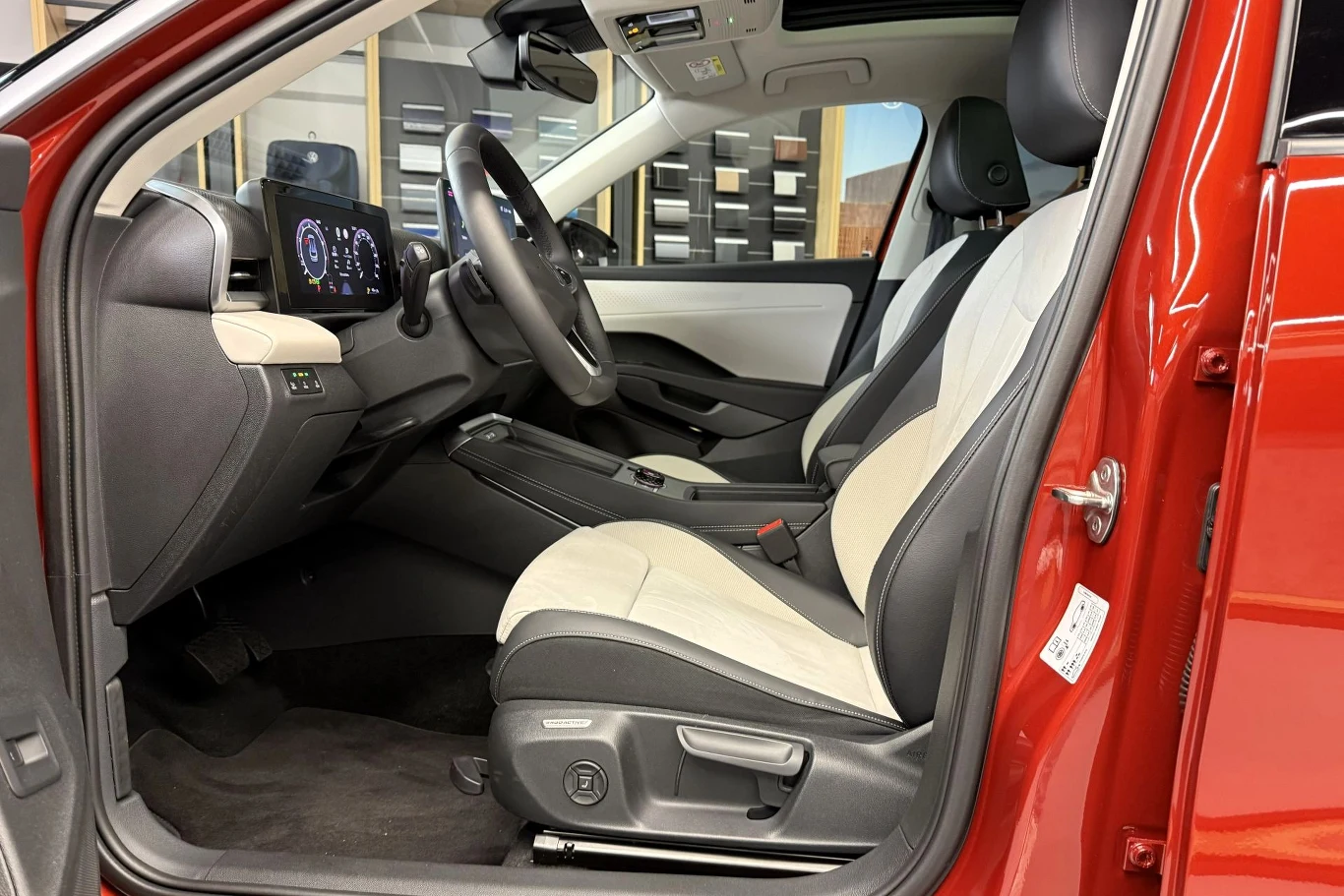 Nowoczesne wnętrze samochodu z czarno-białą tapicerką, elektronicznym panelem zegarów, kierownicą wielofunkcyjną oraz dużym ekranem dotykowym na konsoli centralnej.