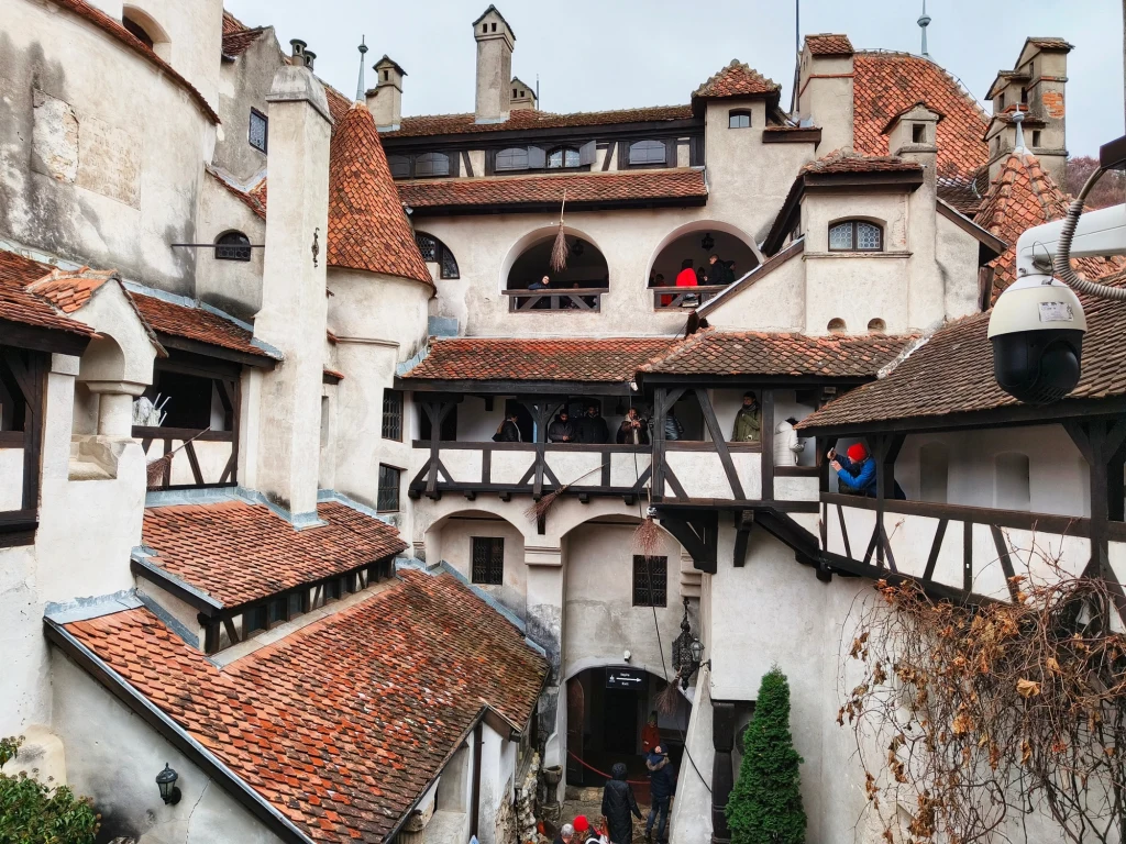 Kamienna twierdza z czerwonymi dachami, białymi ścianami oraz licznymi schodami i balkonami, na których widoczni są turyści podziwiający budowlę, w tle widać otwarte łuki i typowe dla średniowiecznego zamku elementy architektoniczne.