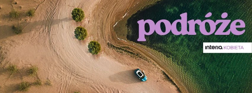 Samochód zaparkowany przy brzegu jeziora na piaszczystej plaży w otoczeniu kilku drzew, z lotu ptaka, widoczny napis podróże oraz logo Interia Kobieta.
