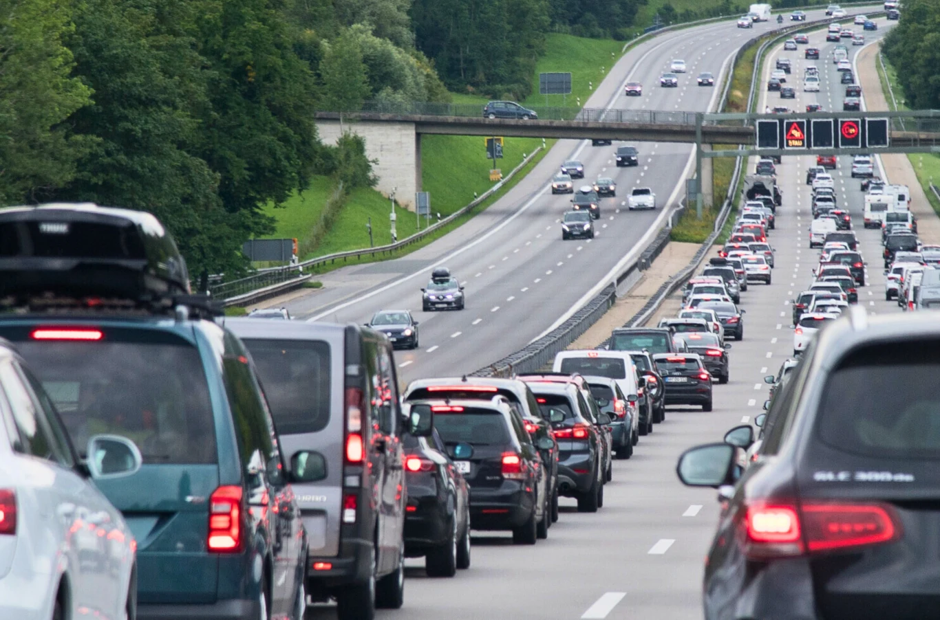 Kary w Niemczech za zjazd z autostrady w korku. Długi korek samochodów na autostradzie, pojazdy stoją zatrzymane na jednym pasie ruchu, po przeciwnej stronie jezdni ruch odbywa się płynnie, w tle widoczne oznakowanie świetlne i zieleń przydrożna.