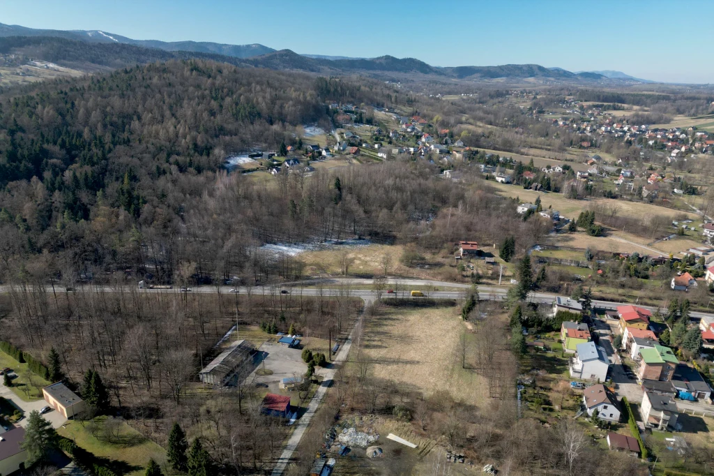 Historyczna trasa przetrwała do dziś w formie m.in. Drogi Krajowej 52. Panorama niewielkiego miasteczka położonego w dolinie, otoczonego wzgórzami porośniętymi lasem. Widoczne są domy jednorodzinne, polany oraz rozległe tereny zielone. W tle rozciągają się zalesione wzgórza i pasmo górskie na horyzoncie.