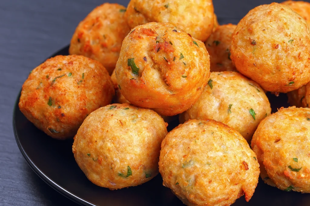 Złociste kulki smażone na głębokim tłuszczu z widocznymi ziołami i przyprawami, ułożone na ciemnym talerzu.