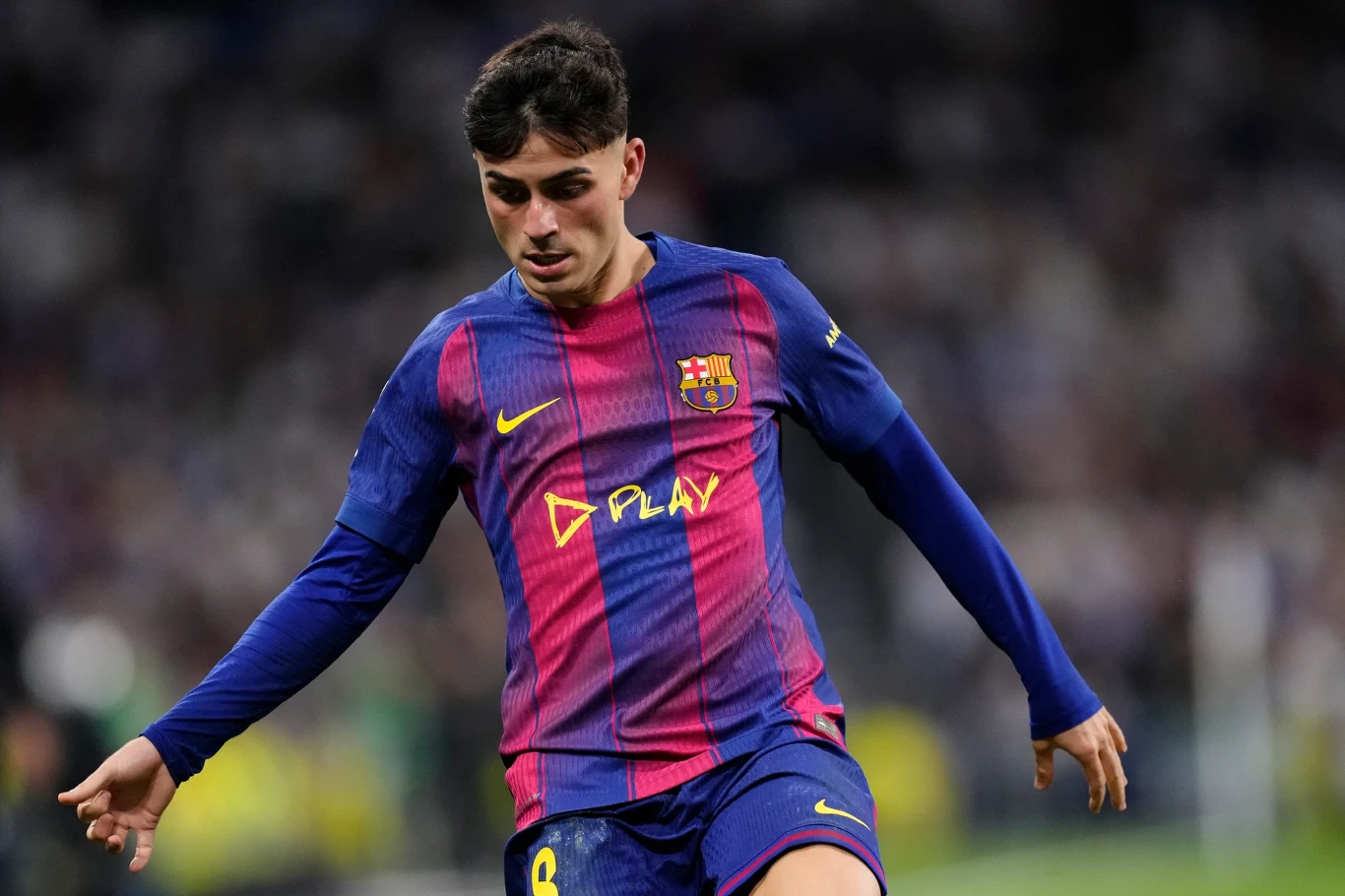 Piłkarz drużyny FC Barcelona w niebiesko-bordowej koszulce z logo sponsora i numerem na krótkich spodenkach podczas meczu piłki nożnej, w dynamicznym ruchu na tle rozmazanej publiczności stadionowej.