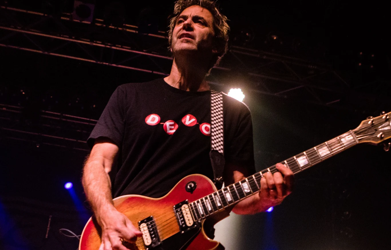 Lagwagon dołącza do składu Lost Generation 2026! Muzyk grający na gitarze elektrycznej na scenie, w tle widoczne oświetlenie koncertowe, ubrany w czarny t-shirt z napisem DEVO, skupiony wyraz twarzy podczas występu.