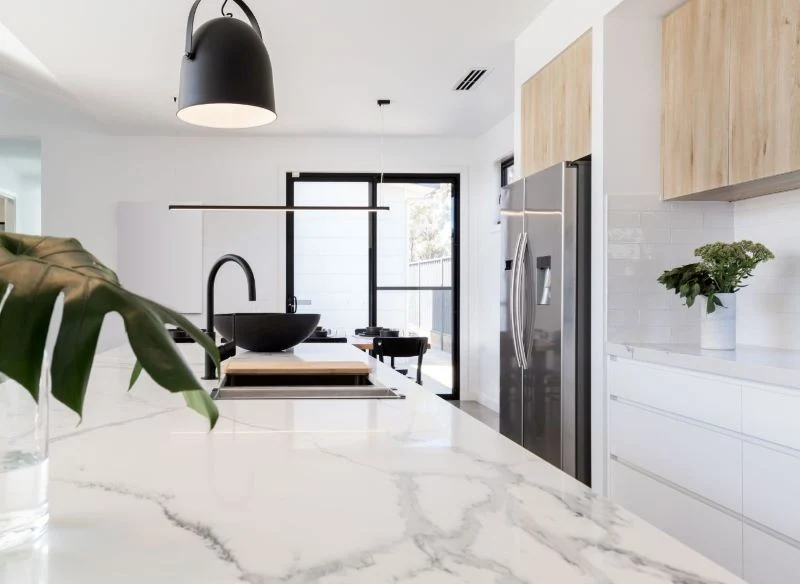 Jasny marmur w kuchni na blacie, do tego jasne meble i ściany z czarnymi dodatkami wyglądają czysto i bardzo estetycznie