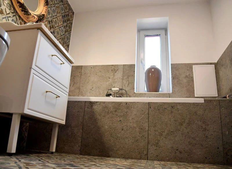 Płytki wykorzystane wokół wanny przeniesiono również płynnie na ściany, tworząc spójną aranżację w wizualnej równowadze