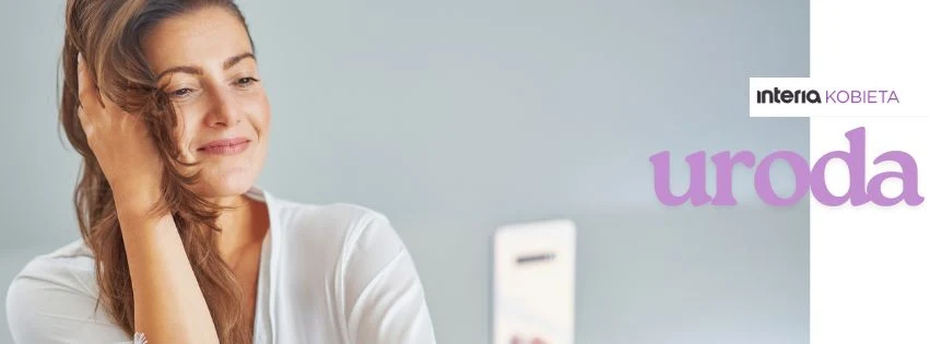 Odkryj tajniki pielęgnacji i poczuj się piękna każdego dnia Uśmiechnięta kobieta o długich, brązowych włosach, delikatnie przykłada dłoń do twarzy, na tle jasnej ściany oraz niewyraźnego białego prostokąta w tle. W górnym rogu widoczne napisy 'interia KOBIETA urodа', wskazujące na tematykę dotyczącą piękna lub ...