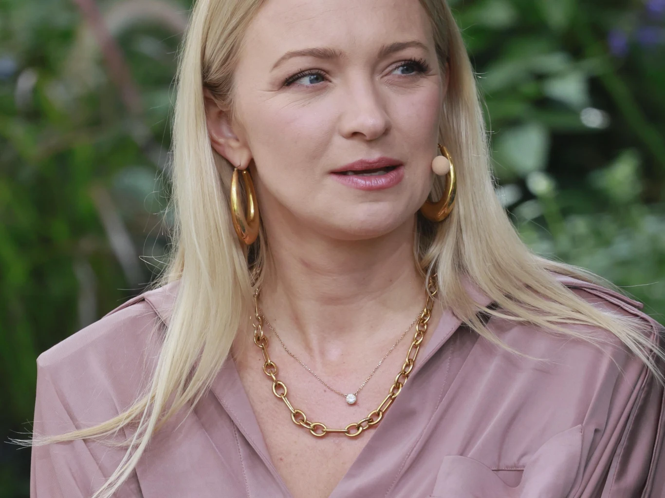 Barbara Kurdej-Szatan stawia sprawę jasno. Zawsze uwielbiała jesienne wieczory. Blondynka w jasnoróżowej bluzce, z długimi włosami, dużymi złotymi kolczykami i złotym łańcuszkiem na szyi, w tle widoczna roślinność.