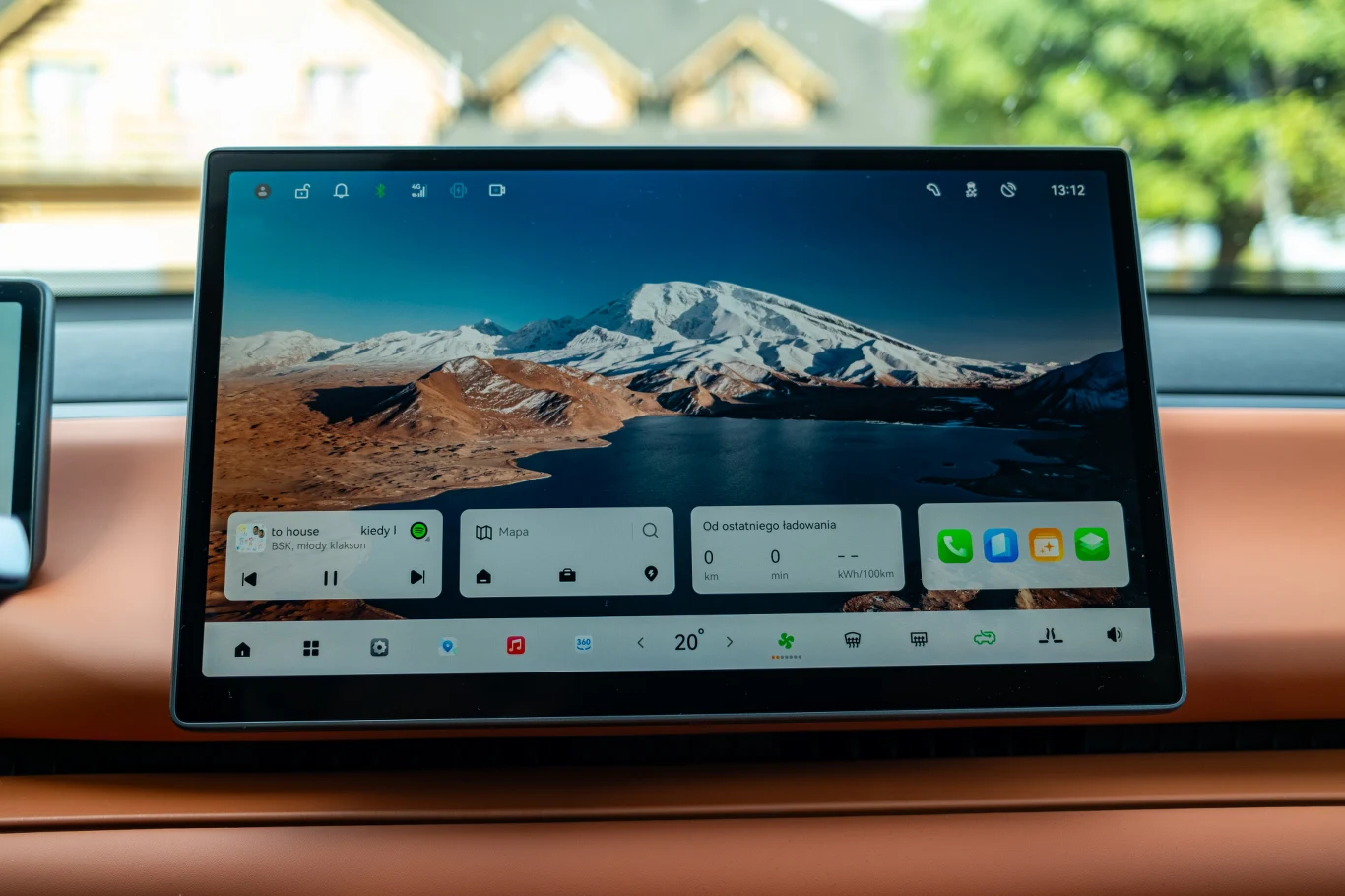Wnętrze nowoczesnego samochodu z dużym panelem dotykowym na konsoli centralnej, na ekranie widoczny interfejs systemu multimedialnego oraz górski krajobraz w tle tapety.