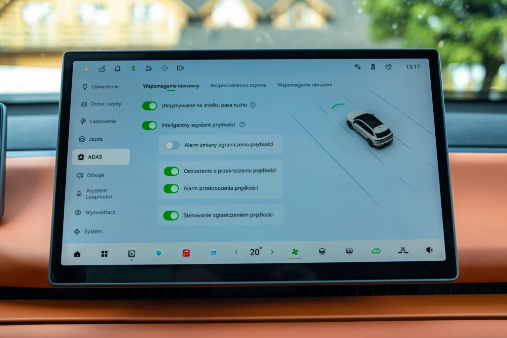 Interaktywny ekran dotykowy systemu ADAS w samochodzie, prezentujący funkcje asystenta jazdy, takie jak utrzymywanie pasa ruchu, ostrzeżenie o przekroczeniu prędkości i inteligentny tempomat. W tle widoczna przednia szyba pojazdu.