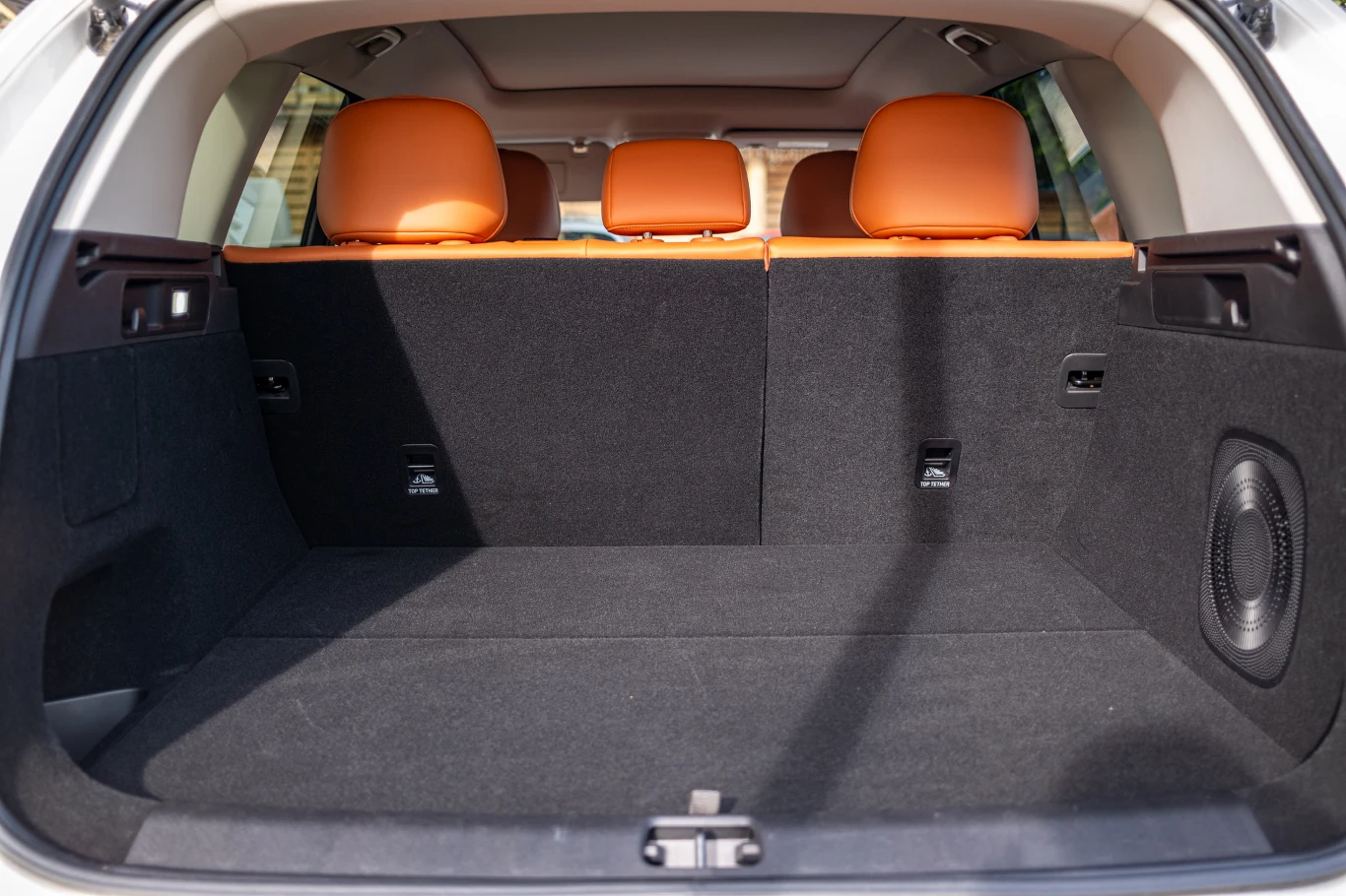 Pojemny bagażnik samochodu z widocznymi pomarańczowymi zagłówkami tylnej kanapy i czarną tapicerką, bez żadnych przewożonych przedmiotów.