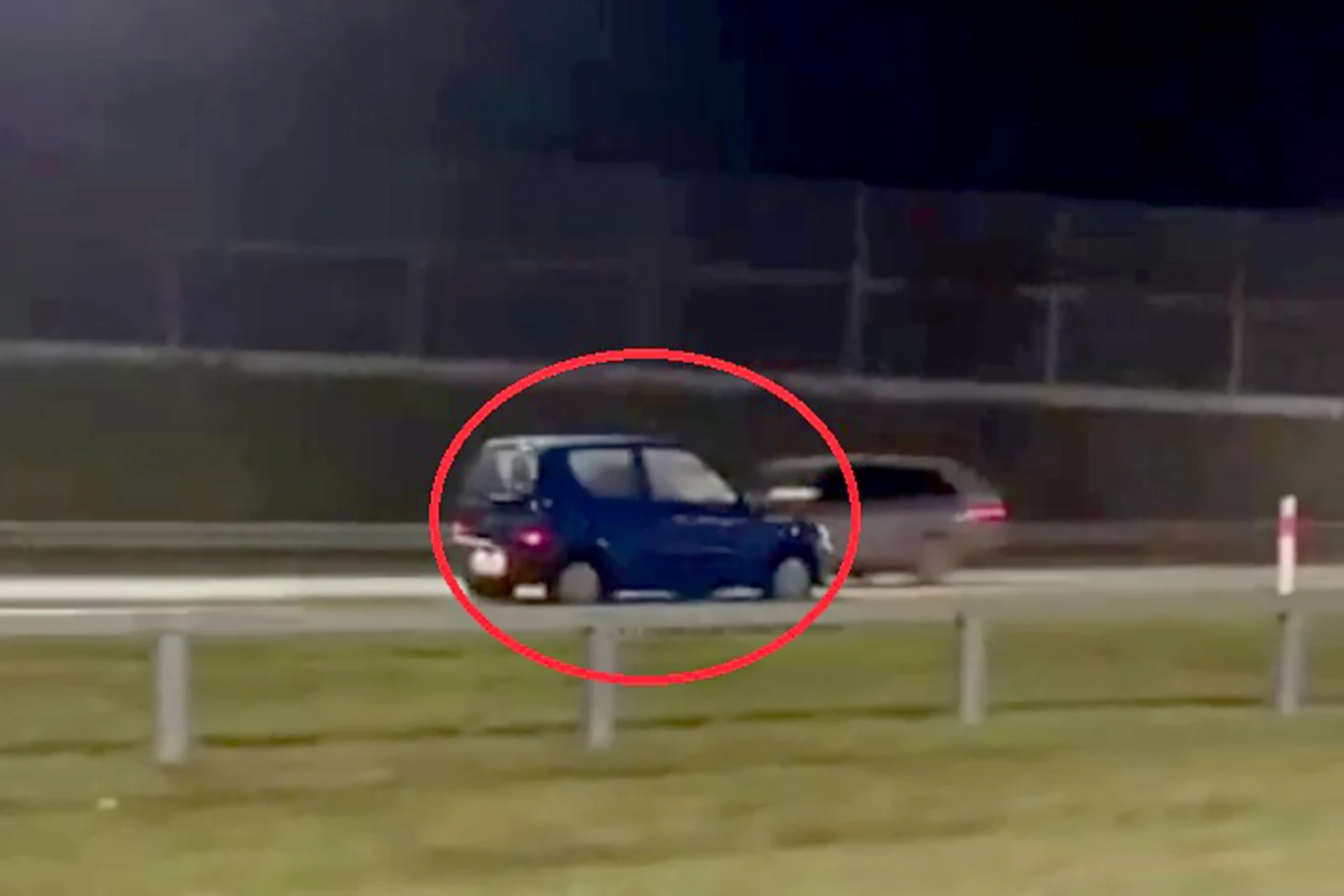 Jechała pod prąd na ekspresówce. Nie wie jak się tam znalazła Nocna scena na drodze szybkiego ruchu, gdzie dwa samochody jadą obok siebie, jeden z pojazdów jest wyraźnie zaznaczony czerwonym okręgiem. W tle widoczny płot oraz trawa przy jezdni.