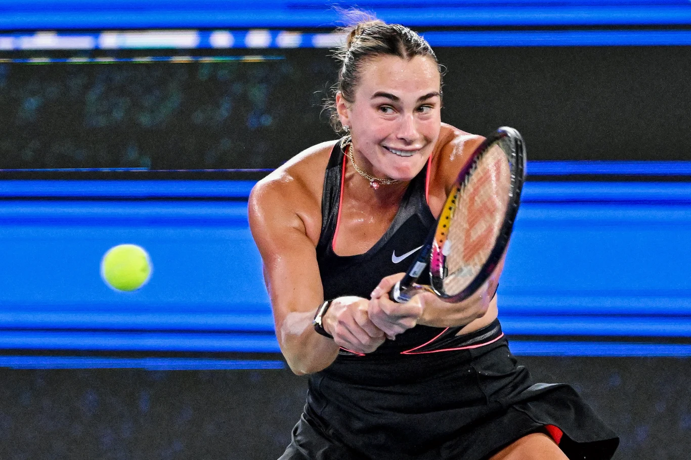 Aryna Sabalenka jest jedną z kandydatek do zwycięstwa w WTA Finals 2025 Tenisistka wykonuje dynamiczne uderzenie piłki podczas meczu tenisowego, skupiona na rozgrywce. W tle kontrastujące, niebieskie linie kortu podkreślają sportowy charakter sceny.