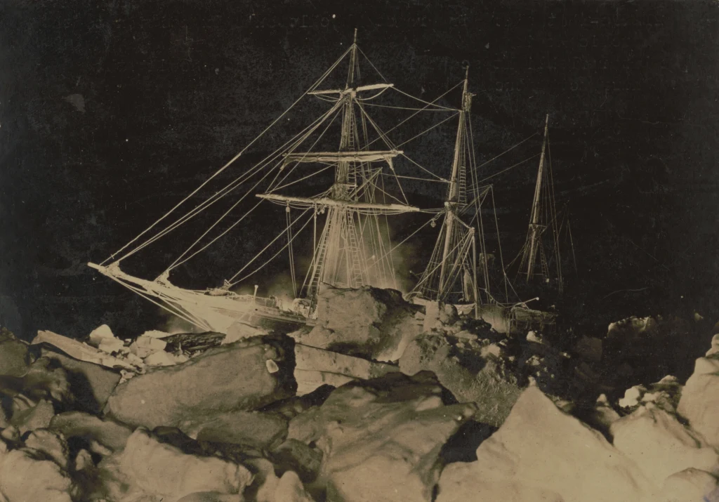 Statek "Endurance" utknął w lodzie Antarktyki w 1915 r. Trójmasztowy żaglowiec otoczony grubymi bryłami lodu, nocna sceneria podkreślająca trudne warunki polarnej ekspedycji.