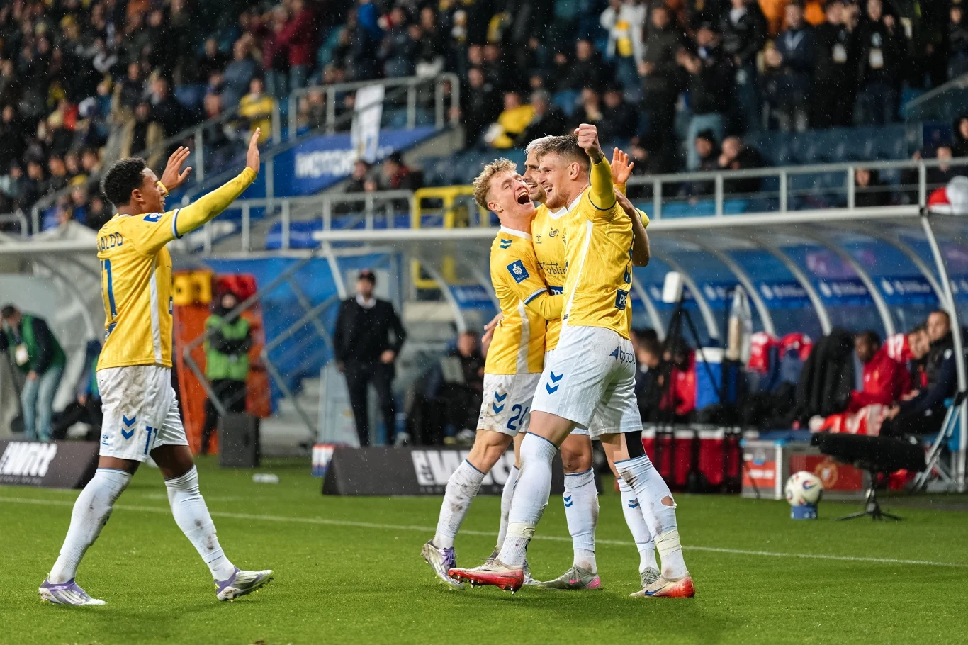 Piłkarze Motoru Lublin w sezonie 2025/2026 PKO BP Ekstraklasy Grupa piłkarzy w żółtych koszulkach świętuje zdobycie gola na murawie stadionu. Radość i entuzjazm zawodników są widoczne, a w tle widać ławkę rezerwowych oraz licznie zgromadzonych kibiców na trybunach.