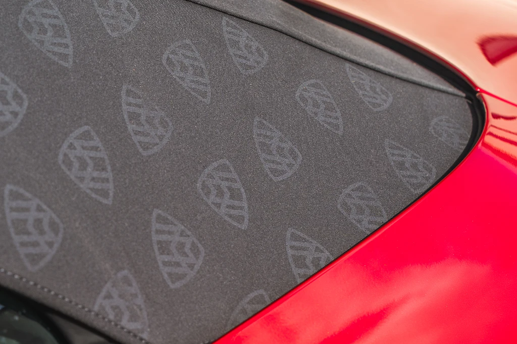 Czarny dach materiałowy z subtelnym wzorem logo marki Maybach na tle czerwonej karoserii samochodu.