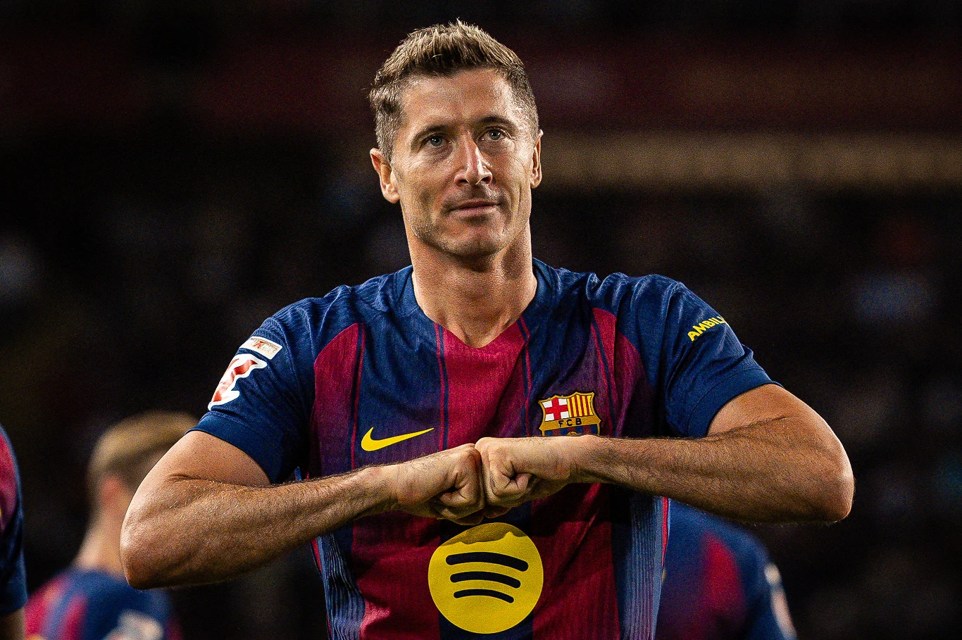 Robert Lewandowski Piłkarz ubrany w koszulkę FC Barcelona, wykonujący gest dłonią, na tle stadionu w czasie meczu, w otoczeniu innych zawodników w podobnych strojach.