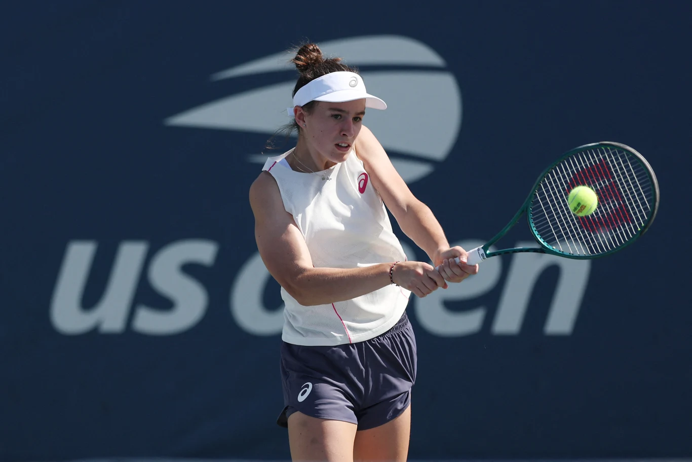 Zawodniczka tenisowa w trakcie meczu, skupiona na odbiciu piłki, trzymająca rakietę oburącz na tle logotypu US Open.