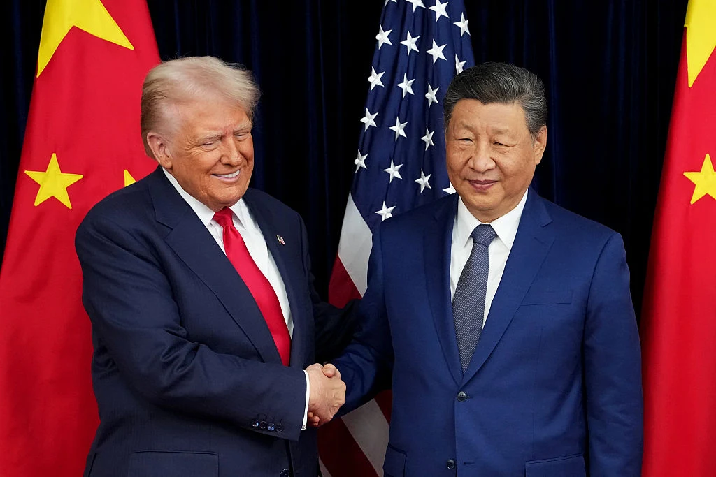 Prezydent USA Donald Trump oraz prezydent Chin Xi Jinping Dwóch mężczyzn w garniturach uśmiecha się i podaje sobie dłonie na tle flag Chin i Stanów Zjednoczonych.