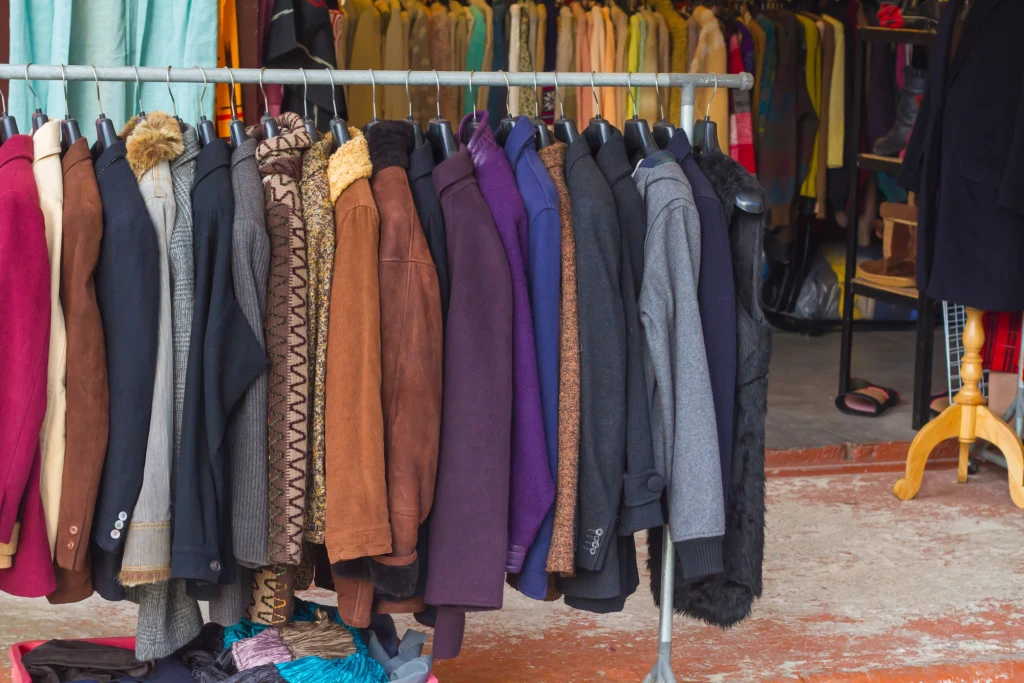 Rząd różnorodnych kurtek, płaszczy i marynarek zawieszonych na metalowym wieszaku, w tle widoczna większa liczba ubrań na innych wieszakach oraz manekin.
