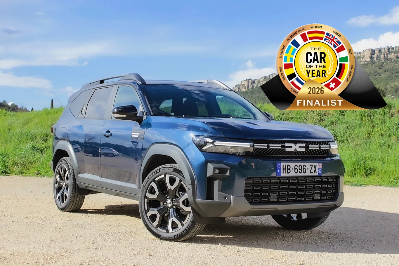 Dacia Bigster znalazła się wśród finalistów Car of the Year 2026 Nowoczesny SUV w kolorze niebieskim zaparkowany na żwirowej nawierzchni, w tle zielona trawa i skały. Obok pojazdu znajduje się odznaka informująca o tytule finalisty międzynarodowego konkursu Car of the Year 2026.